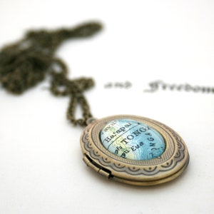 May include: A brass locket necklace with a map of Tonga inside. The locket has a scalloped edge and a hinged closure.