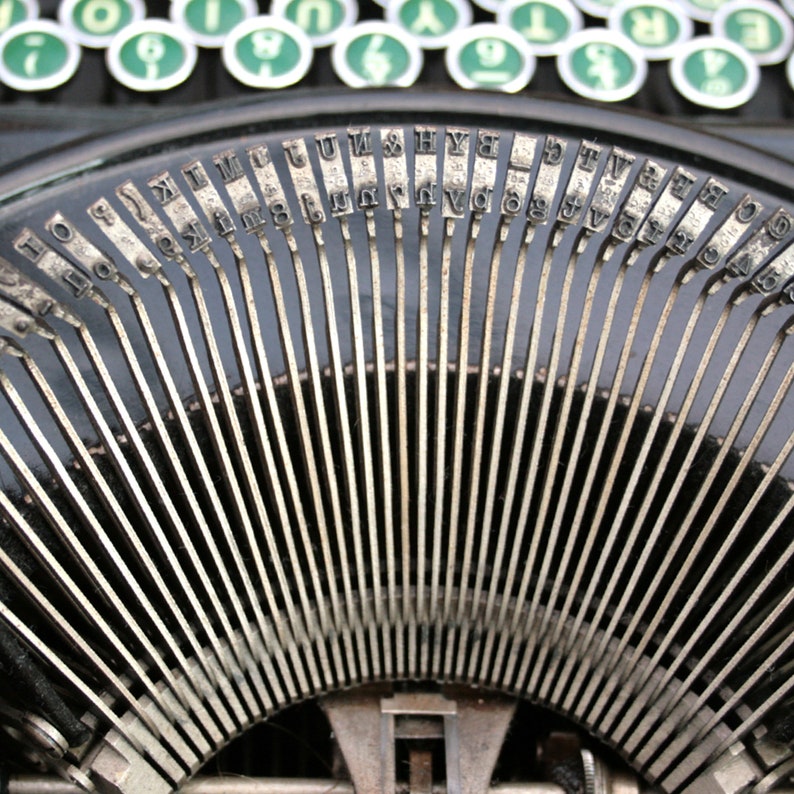 May include: Close-up of a vintage typewriter with metal keys arranged in a semi-circle. The keys are labeled with letters, numbers, and symbols.