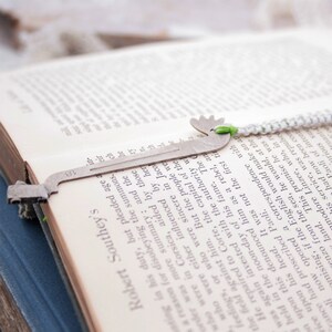 May include: A silver bookmark shaped like a deer with a green and white braided cord attached. The bookmark is resting on a page of an open book with text printed on the page. The text on the page reads "Robert Southey's".