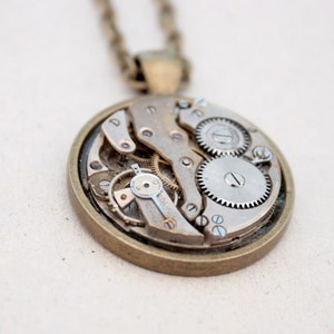 May include: A silver and bronze necklace with a round pendant featuring exposed clockwork gears.