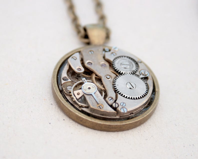 May include: A silver and bronze necklace with a round pendant featuring exposed clockwork gears.