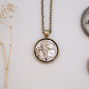 May include: A gold necklace with a round pendant featuring a detailed clockwork design. The pendant is made of brass and has a clear glass face revealing the intricate gears inside.