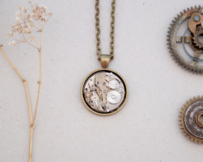 May include: A gold necklace with a round pendant featuring a detailed clockwork design. The pendant is made of brass and has a clear glass face revealing the intricate gears inside.