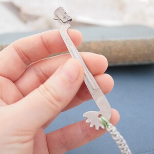 May include: A silver metal tool with a serrated edge and a small gear at the end. The tool is being held in a hand.