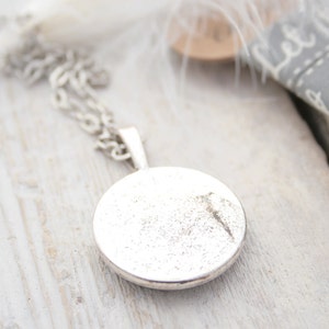 May include: A silver necklace with a round pendant. The pendant is smooth and has a slightly textured surface.