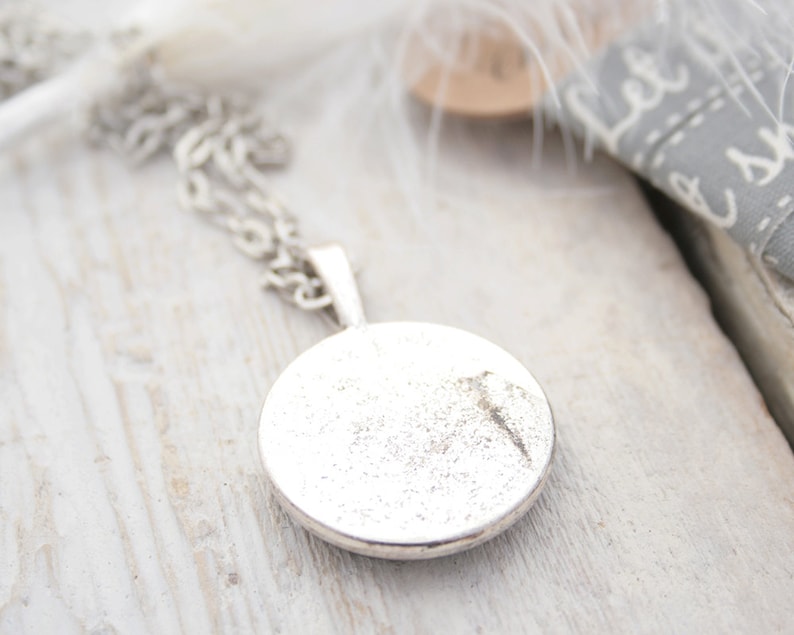 May include: A silver necklace with a round pendant. The pendant is smooth and has a slightly textured surface.