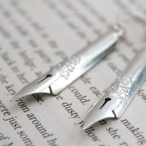 Puede incluir: Un par de pendientes de plata con forma de plumines de pluma vintage. Los plumines tienen un delicado dise&ntilde;o floral.