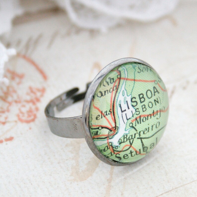 May include: A silver ring with a round glass cabochon featuring a vintage map of Lisbon, Portugal. The map is green and orange with the text "LISBOA (LISBON)" and "Setubal" visible.