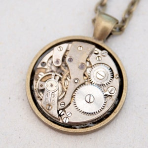 May include: A round, bronze pendant necklace with a clear glass face revealing the intricate workings of a vintage watch movement.