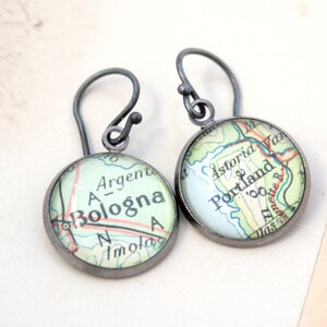 May include: A pair of silver dangle earrings with map-themed glass cabochons. One earring features a map of Bologna, Italy, with the text "A-Bologna" visible. The other earring features a map of Portland, Oregon, with the text "Astoria" and "Portland" visible.