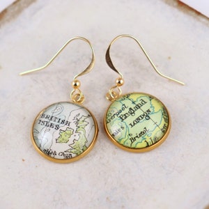 May include: Gold dangle earrings with a round glass charm featuring a vintage map of the British Isles. The map shows the text "British Isles" and "Irish Chan."