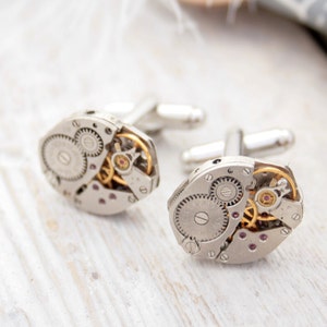 May include: A pair of silver cufflinks with intricate gold gears and a silver finish. The cufflinks are made from repurposed watch parts.