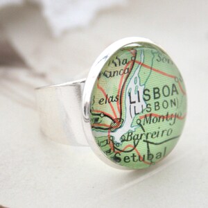May include: A silver ring with a round glass cabochon featuring a vintage map of Lisbon, Portugal. The map shows the city's name in both Portuguese and English, "LISBOA (LISBON)", along with surrounding towns and geographical features.