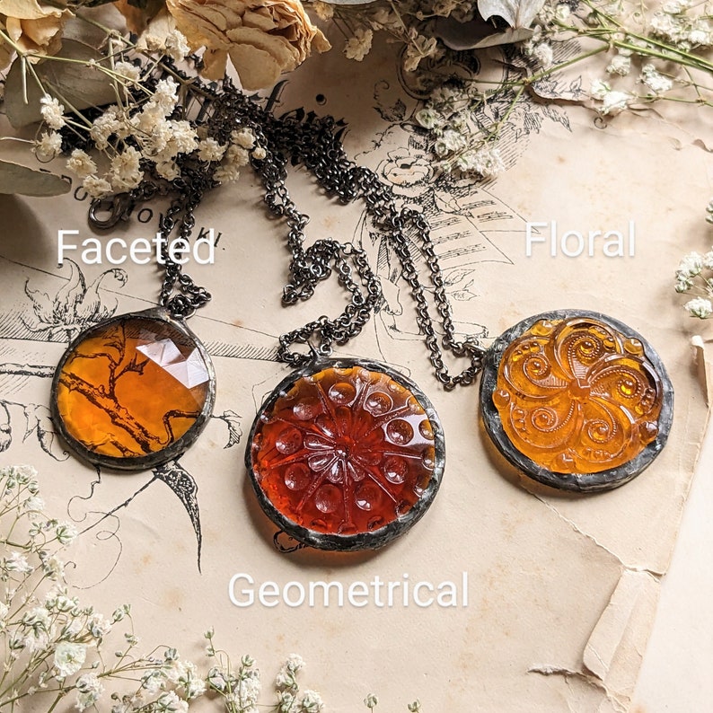 Puede incluir: Tres colgantes de vidrio &aacute;mbar en una cadena plateada. Los colgantes son redondos y tienen diferentes dise&ntilde;os: facetado, floral y geom&eacute;trico.