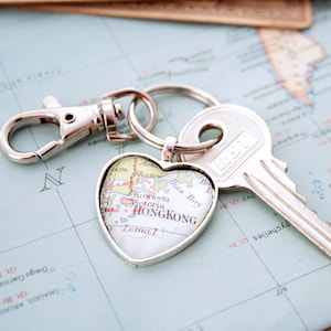 May include: A silver keychain with a heart-shaped pendant featuring a map of Hong Kong. The keychain includes a key and a clasp. The map pendant has the word "HONGKONG" printed on it.