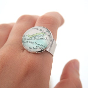 May include: A silver ring with a round glass top featuring a vintage map of Grand Bahama Island. The map shows the location of Freeport and North West Providence.