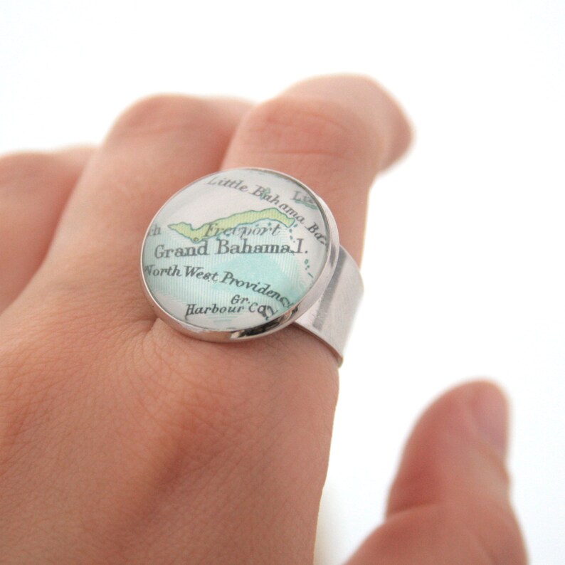 May include: A silver ring with a round glass top featuring a vintage map of Grand Bahama Island. The map shows the location of Freeport and North West Providence.