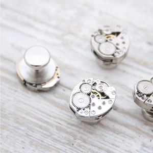 May include: Four silver cufflinks with intricate clockwork designs. Each cufflink features a different arrangement of gears and cogs, creating a unique and stylish look.