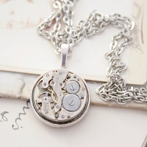May include: A silver necklace with a round pendant featuring a vintage watch movement. The pendant is about 1.5 inches in diameter and has a silver chain.