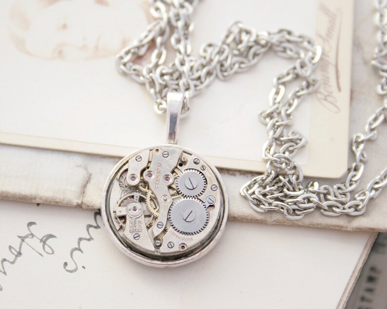 May include: A silver necklace with a round pendant featuring a vintage watch movement. The pendant is about 1.5 inches in diameter and has a silver chain.