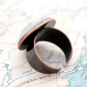 May include: A copper ring with a blue and white glass cabochon. The ring is on a map.