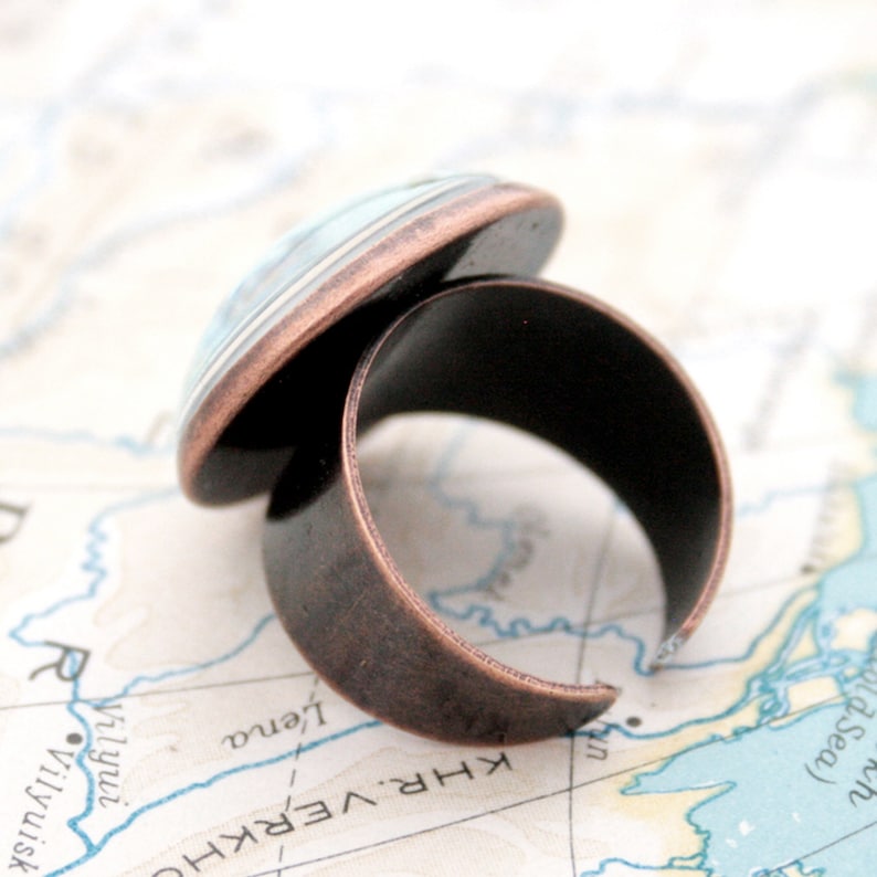 May include: A copper ring with a blue and white glass cabochon. The ring is on a map.