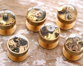 May include: Six gold-toned metal cufflinks with clear resin tops. Each cufflink features a different arrangement of small, gold-colored gears.
