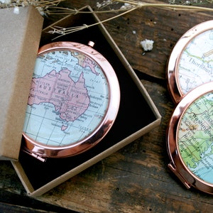 Op de afbeelding: Een set van drie ronde, koperkleurige compact spiegels met vintage kaartontwerpen. De kaarten tonen Australië, de Verenigde Staten en een regio van Engeland.