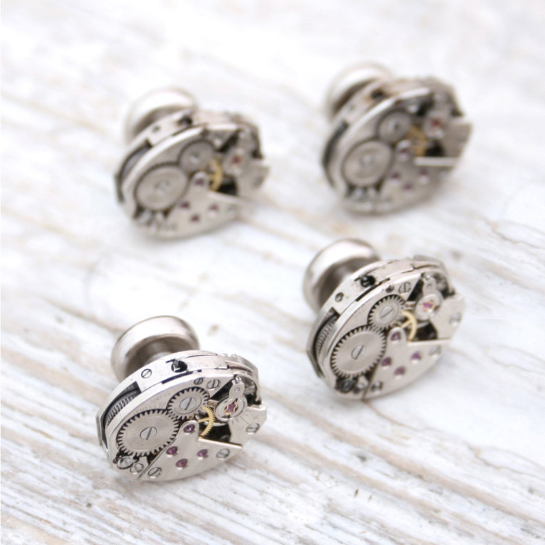 May include: Four silver cufflinks with intricate clockwork designs. Each cufflink features a circular face with exposed gears and a silver finish.