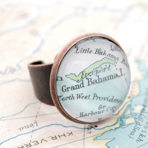 May include: A copper ring with a glass cabochon featuring a vintage map of Grand Bahama Island. The map shows the location of Freeport and North West Providence.