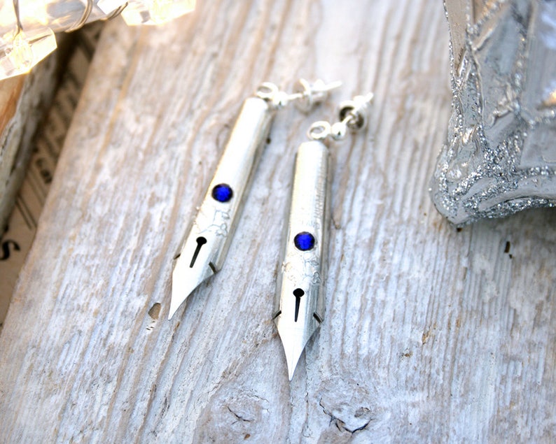 May include: A pair of silver earrings shaped like calligraphy nibs with blue gemstone accents.