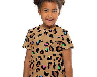 May include: A tan-colored t-shirt featuring a leopard print design with black spots and colorful accents. The shirt has a crew neck and short sleeves. The colorful accents include pink, blue, green, and orange.
