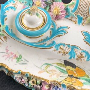May include: A porcelain inkwell set with a blue and gold design. The inkwell is decorated with flowers and a butterfly.