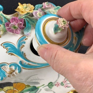 May include: A porcelain inkwell with a floral design and a butterfly. The inkwell has a blue and gold trim and a removable lid with a floral design.