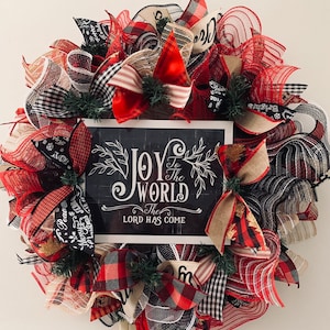 May include: A Christmas wreath with red, black, and white plaid ribbon, burlap ribbon, and red mesh. The wreath has a sign that says "Joy to the World The Lord Has Come".