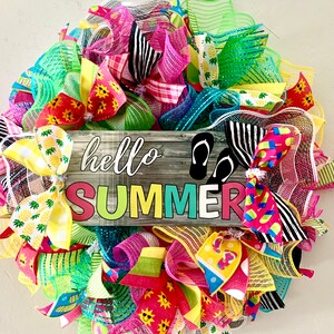 May include: A summer wreath with a wooden sign that says "hello summer". The wreath is made of mesh and ribbon in various colors, including pink, green, yellow, and blue. There are also flip flops and pineapple designs on the wreath.