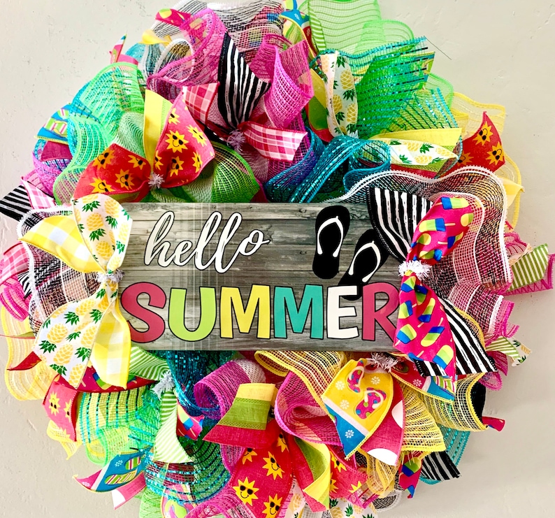 May include: A summer wreath with a wooden sign that says "hello summer". The wreath is made of mesh and ribbon in various colors, including pink, green, yellow, and blue. There are also flip flops and pineapple designs on the wreath.