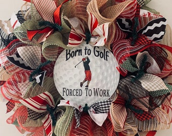 May include: A golf-themed wreath with red, white and green mesh, burlap and ribbon. The wreath features a white golf ball with a golfer and the text "Born to Golf Forced to Work".