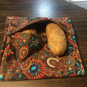 May include: Two brown potatoes in a colorful fabric pouch with a paisley pattern. The pouch has a brown flap that is folded over the potatoes.