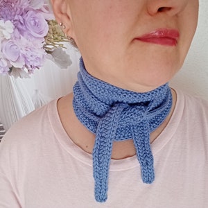 Może przedstawiać: Jasno niebieski dzianinowy ochraniacz szyi z zawiązanym węzłem z przodu.