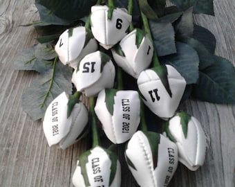 May include: A bouquet of white roses with green leaves. Each rose is decorated with a black and white design and the text "CLASS OF 2021". Some roses also have numbers on them, including 1, 6, 11, and 15.