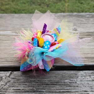 May include: A colourful hair bow with pink, yellow, blue and white ribbons, a pink and white polka dot ribbon, and a pink button with the text "It's a Girl" in white.