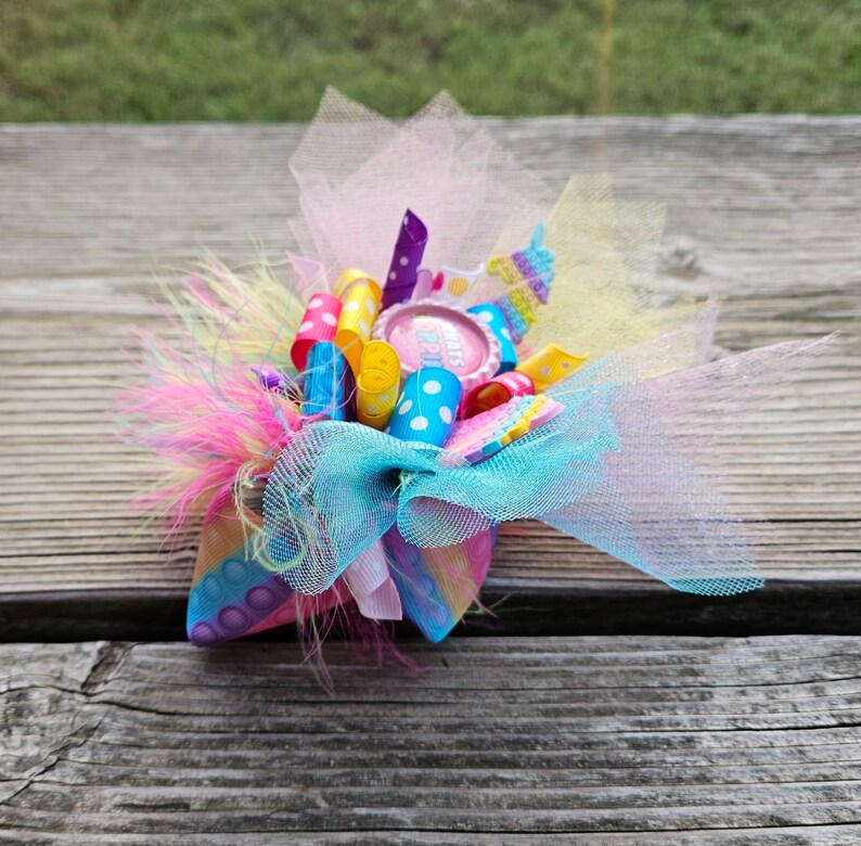 May include: A colourful hair bow with pink, yellow, blue and white ribbons, a pink and white polka dot ribbon, and a pink button with the text "It's a Girl" in white.