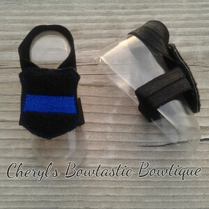 May include: A pair of black dog booties with a blue embroidered line on one bootie. The booties are on a wooden surface.
