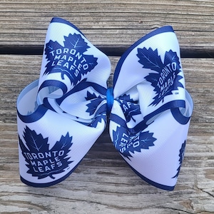 May include: A white and blue bow with the Toronto Maple Leafs logo. The bow is made of ribbon and has a blue center.