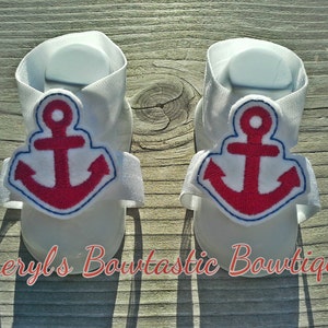May include: A pair of white baby sandals with red anchor embroidery. The sandals have adjustable straps and are perfect for summer.
