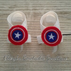 May include: A pair of white baby booties with red, white, and blue Captain America shield appliques.