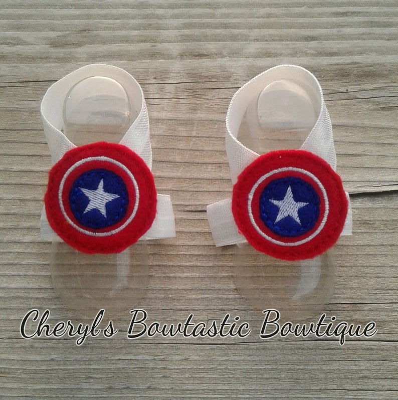 May include: A pair of white baby booties with red, white, and blue Captain America shield appliques.