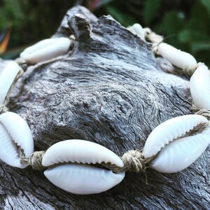 May include: A white shell necklace with natural twine string. The necklace is made of cowrie shells and is a popular style of jewelry.