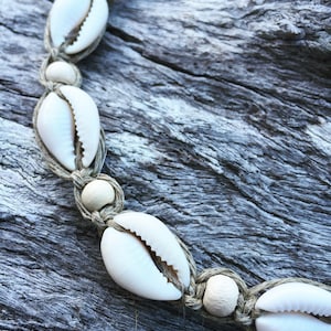 May include: A white shell necklace with brown string and white beads. The necklace is on a wooden surface.